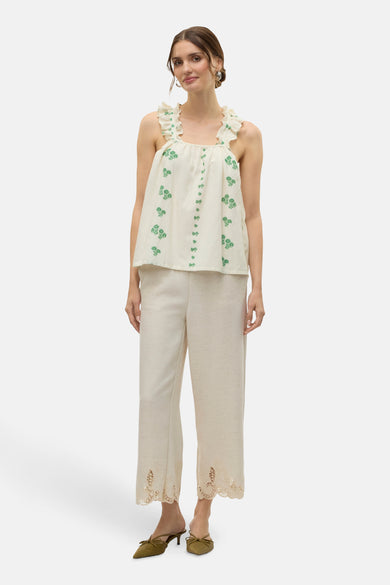 Ecru mouwloze blouse van VERO MODA®, met groene bloemenmotieven en ruches aan de schouders, gecombineerd met beige broek en groene muiltjes.