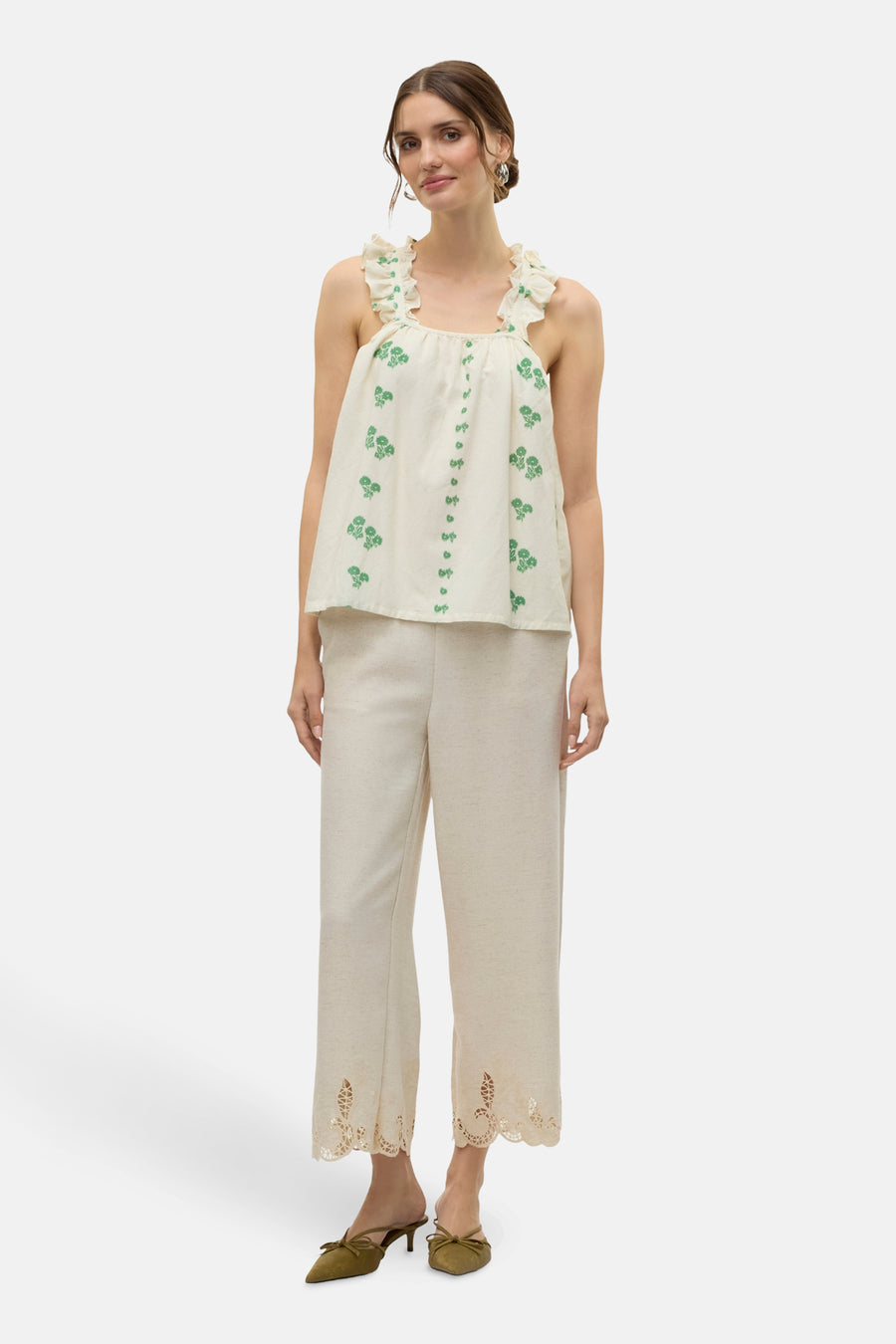 Ecru mouwloze blouse van VERO MODA®, met groene bloemenmotieven en ruches aan de schouders, gecombineerd met beige broek en groene muiltjes.