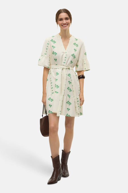 Beige kleedje met korte mouwen van VERO MODA, met groene bloempatronen, riem in de taille en bruine laarzen.
