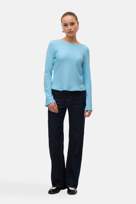 Blauw T-shirt met lange mouwen van VERO MODA®, met een geweven textuur, gecombineerd met donkere jeans en zwarte schoenen.
