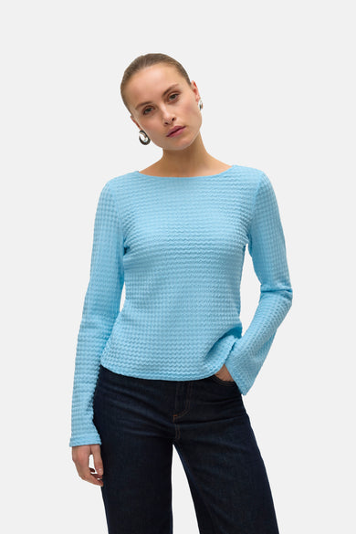 Blauw T-shirt met lange mouwen van VERO MODA met wafeltextuur, gecombineerd met donkere jeans en zilveren oorbellen.
