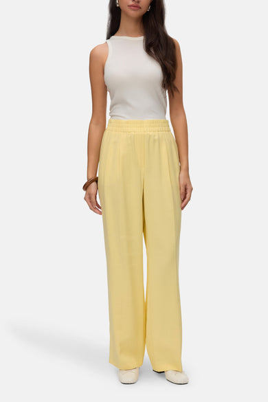 Gele broek van Vero Moda, gecombineerd met een mouwloze witte top en een houten armband.
