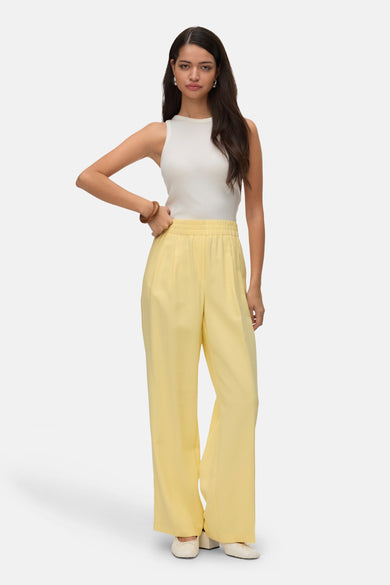 Gele broek van VERO MODA®, gecombineerd met een witte top en beige schoenen.