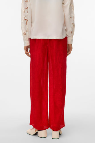 Rode broek van VERO MODA, met een crêpe textuur en wijde pijpen, gecombineerd met een ecru blouse met kanten mouwen.
