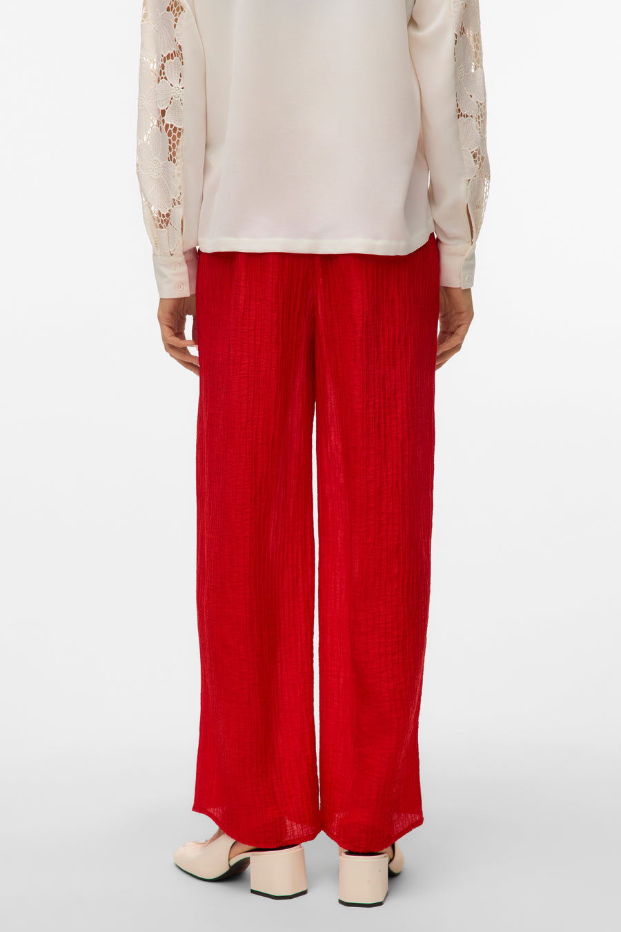 Rode broek van VERO MODA, met een crêpe textuur en wijde pijpen, gecombineerd met een ecru blouse met kanten mouwen.
