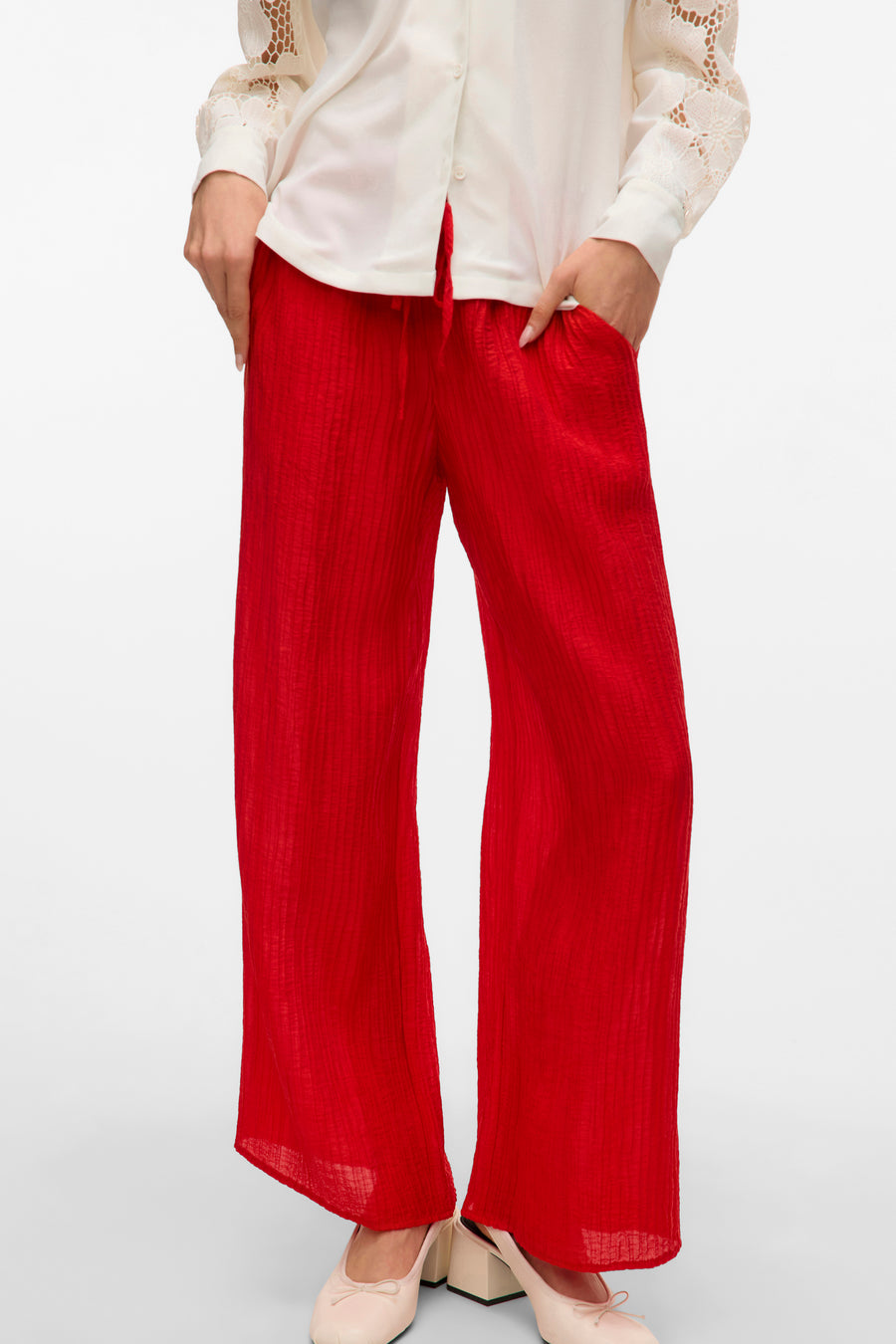 Rode broek van VERO MODA, met wijd uitlopende pijpen en textuur, gecombineerd met een witte blouse en platte schoenen.
