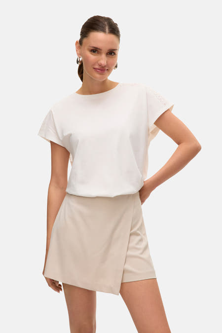 Wit T-shirt met korte mouwen van VERO MODA, met kanten details op de mouwen, gedragen met een beige rokje.
