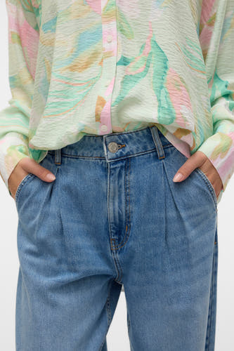 Jeans special fit van blauw denim van VERO MODA, met plooien en steekzakken, gecombineerd met een blouse met abstracte print.