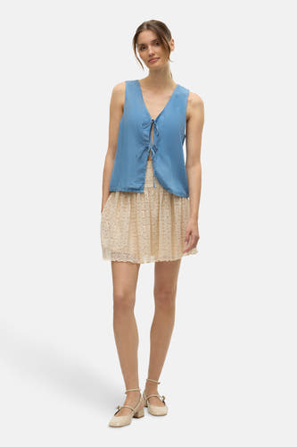 Blouse in blauw van VERO MODA®, met strikdetail en gecombineerd met een beige kanten rok en Mary Jane schoenen.
