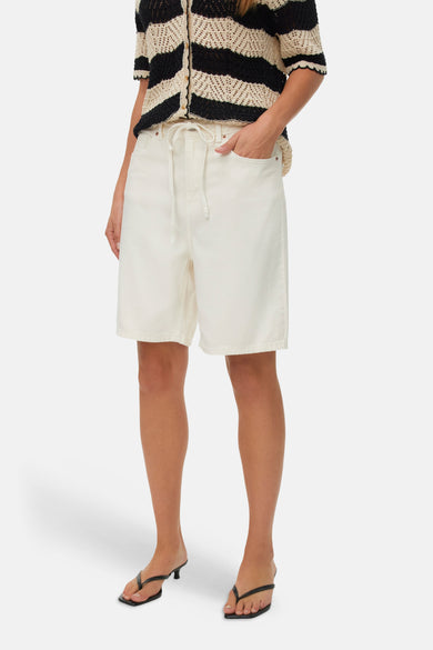 Short écru de VERO MODA®, combiné avec un pull rayé et des tongs noires.