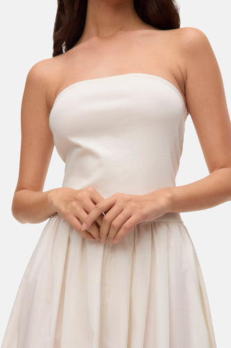Vrouw in witte strapless jurk met geplooide rok, handen gevouwen.