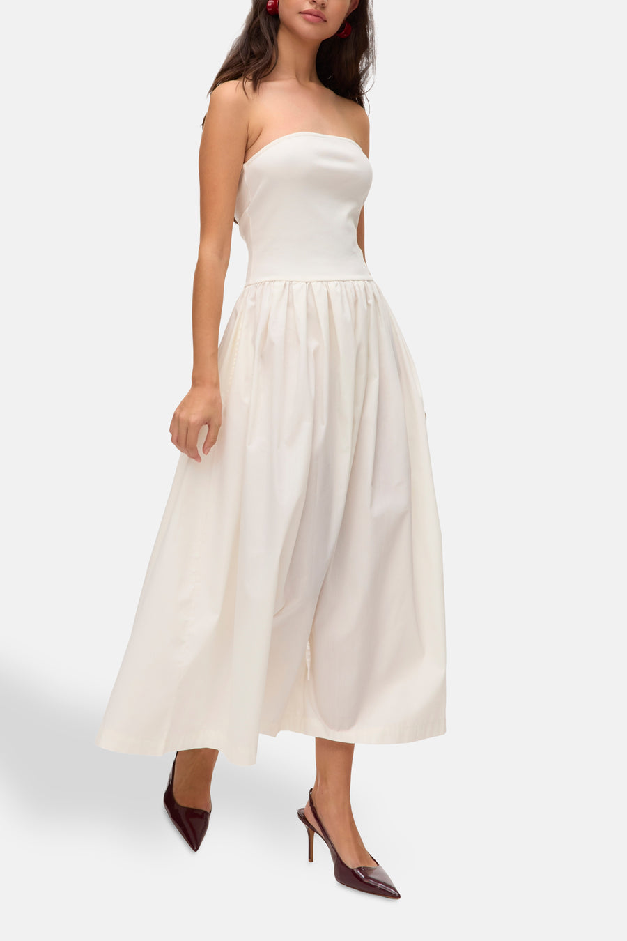Vrouw in een witte, strapless jurk met rode oorbellen en rode pumps.