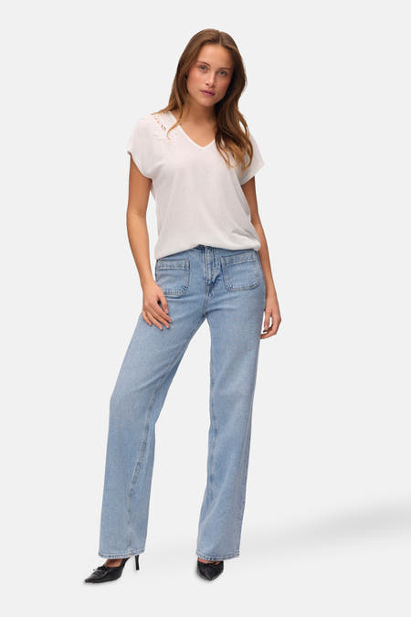 Wit T-shirt met korte mouwen van VERO MODA®, met kanten details bij de halslijn, gecombineerd met een blauwe jeans en zwarte schoenen.