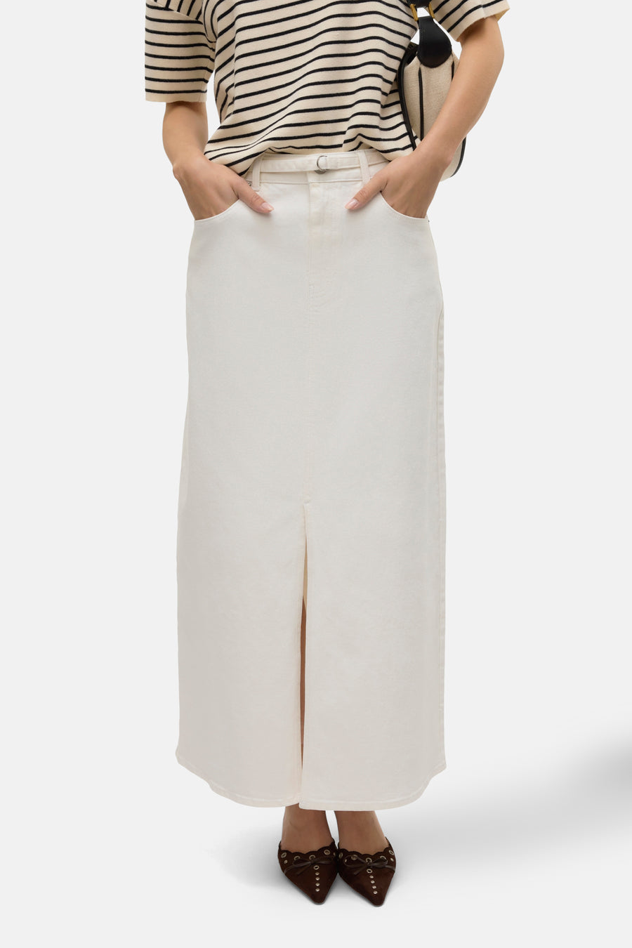 Longue robe blanche de VERO MODA, avec une fente, combinée à une chemise rayée et des chaussures marron.