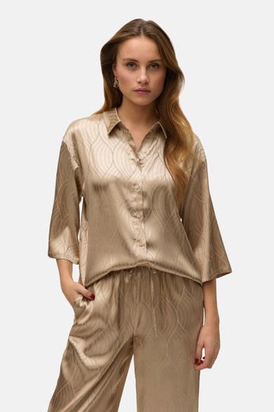 Beige hemd met korte mouwen van VERO MODA, met een golvend patroon en gouden oorbellen.
