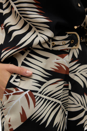 Short noir de VERO MODA, avec motif feuille, boucle d'attache en or et main dans la poche.