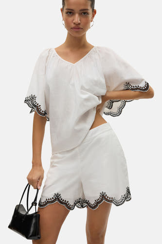 Blouse blanche VERO MODA avec bordure brodée, associée à une blouse blanche et un sac main noir.