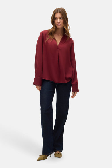 Rode blouse met lange mouwen van VERO MODA, gecombineerd met donkere jeans en olijfgroene pumps.