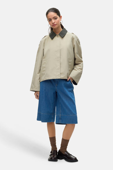 Ecru korte jas van VERO MODA, met een donkere kraag, gecombineerd met een wijde denim broek en bruine loafers.

