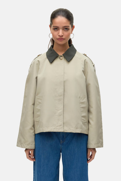 Ecru jas van VERO MODA met donkergroene kraag en zichtbare blauwe jeans.
