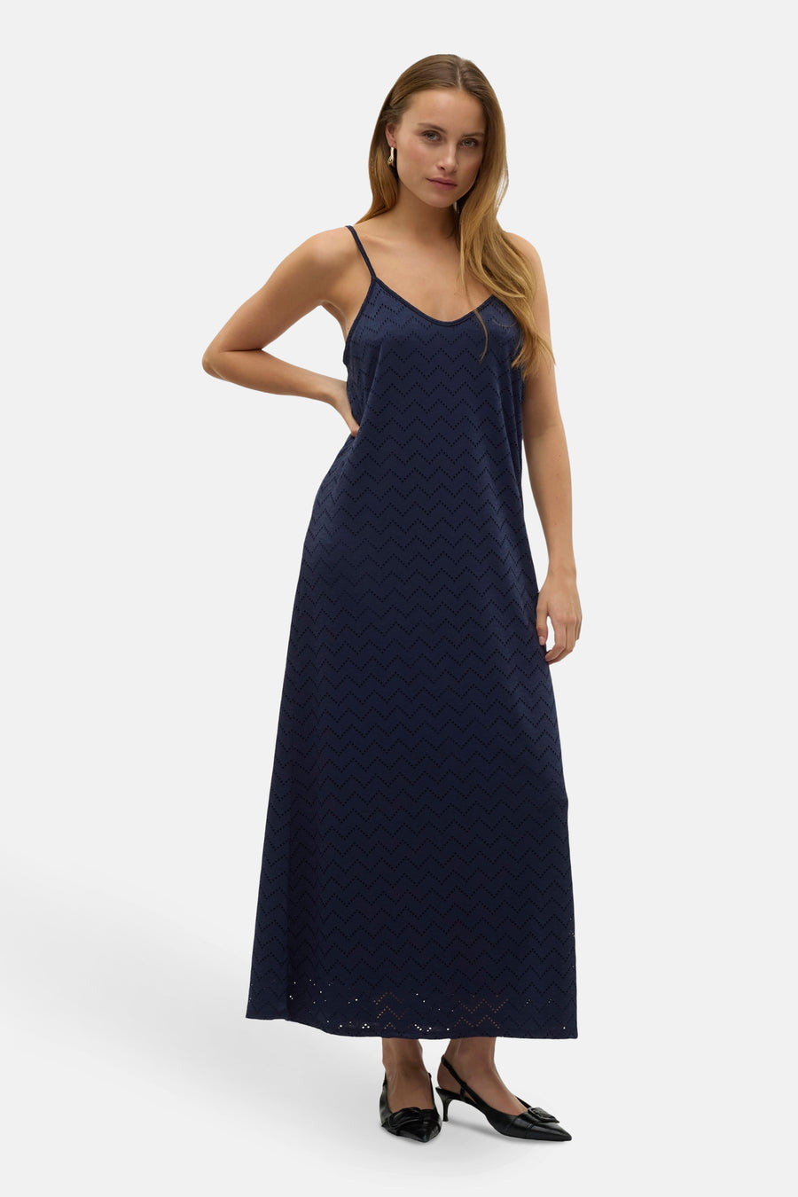 Donkerblauwe kleedje zonder mouwen van VERO MODA®, met een geperforeerd zigzagpatroon, gedragen met zwarte pumps.
