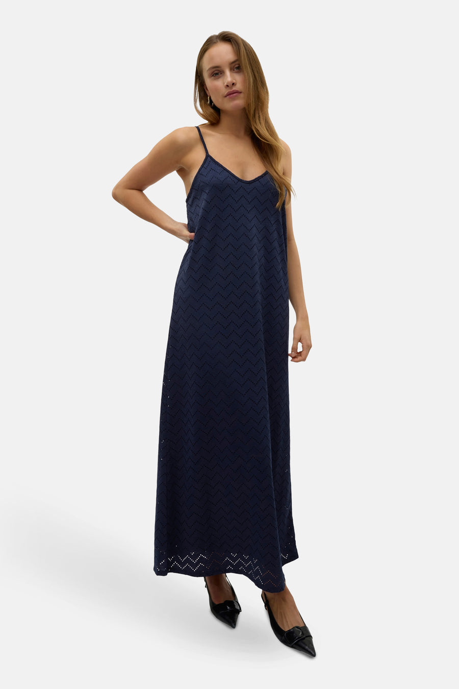 Donkerblauwe mouwloze jurk van VERO MODA, met een zigzagpatroon, gecombineerd met zwarte pumps.

