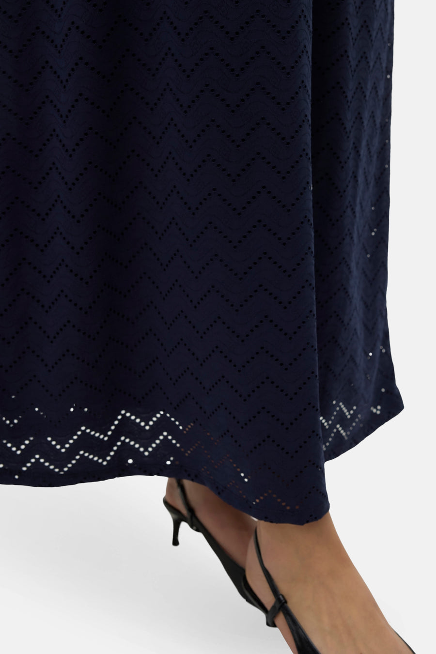 Donkerblauwe mouwloze jurk van VERO MODA, met zigzagpatroon en broderie details, gecombineerd met zwarte hakken.
