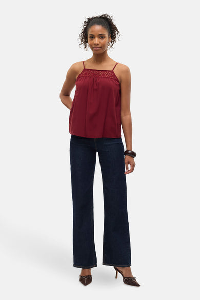 Mouwloze bordeauxrode blouse van Vero Moda, met kanten details en gecombineerd met donkere jeans en bruine hakken.
