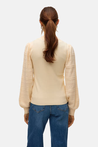 Veste écru avec col rond de VERO MODA, manches longues avec des détails ajourés, vue d'en arrière sur une femme en jeans.