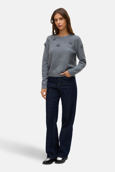 Grijze trui met ronde hals van Vero Moda, afgewerkt met bloemendetails, gecombineerd met een donkerblauwe jeans en zwarte schoenen.