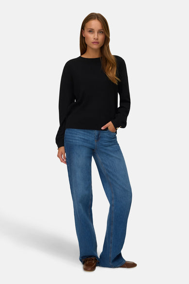 Pull noir avec col rond de VERO MODA, à longues manches et porté avec des jeans bleus et des chaussures marrons.