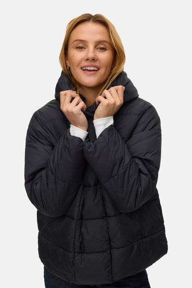 Zwarte korte jas van VERO MODA®, met lange mouwen en een capuchon, gedragen door een lachende vrouw.
