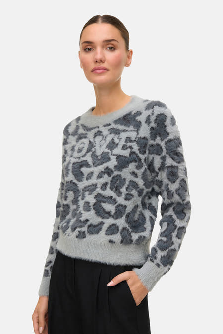 Grijze trui met ronde hals van VERO MODA, voorzien van een luipaardprint met 'LOVE'-opdruk, gecombineerd met een zwarte broek.
