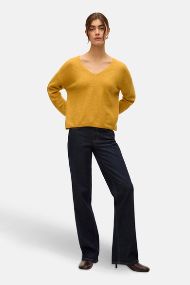 Gele V-hals trui van VERO MODA, gecombineerd met donkere jeans en bruine schoenen.
