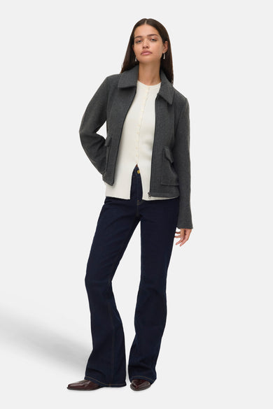 Grijze korte jas van VERO MODA®, met lange mouwen, gedragen over een wit vest met donkere jeans.
