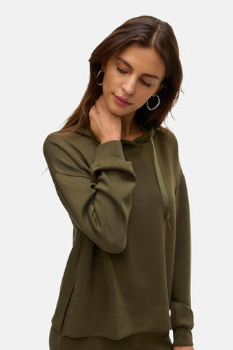 Pull-over vert de VERO MODA MOD cap, avec une cord et des longs manches, porté avec des boucles d'oreilles en argent.