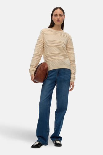 Gilet beige avec col rond de VERO MODA, doté de perforations décoratives et porté avec des jeans bleus et des chaussures noires.