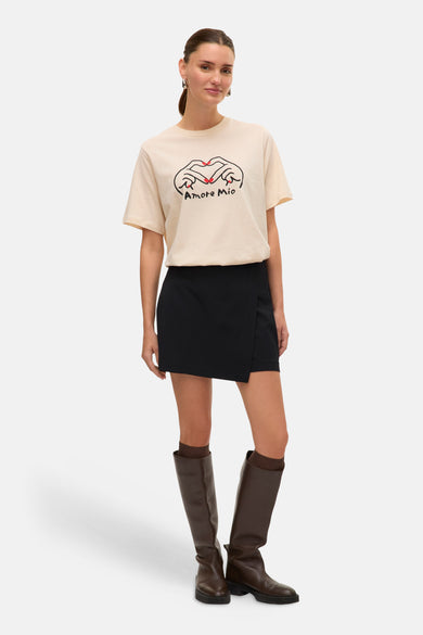 Zwarte skort van VERO MODA, met een overslagdetail en gecombineerd met bruine laarzen en een crèmekleurig T-shirt.