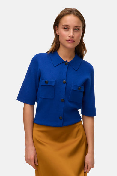 Blauw gilet van VERO MODA, met knopen en zakken, gecombineerd met een goudkleurige rok.
