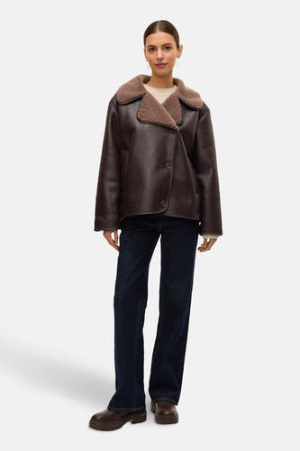 Bruine korte jas van VERO MODA, met lammy kraag, gedragen over een crèmekleurige trui, in combinatie met donkerblauwe jeans en bruine laarzen.