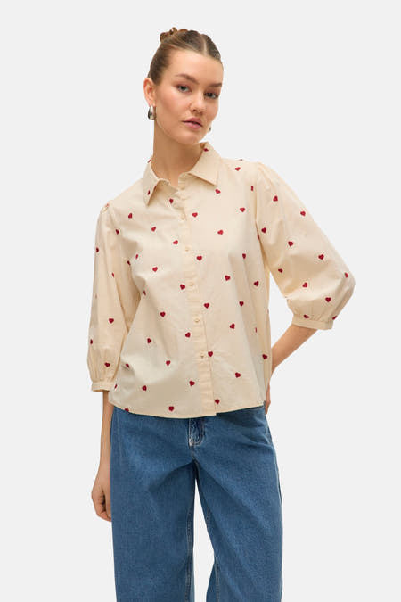 Beige overhemd met korte mouwen van Vero Moda, met een all-over rood hartjespatroon, gecombineerd met blauwe jeans.