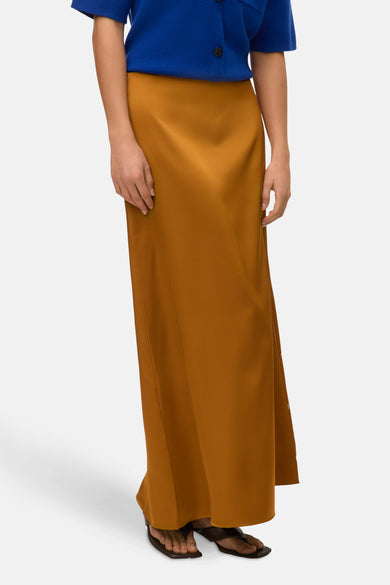 Gouden lange rok van VERO MODA, gecombineerd met een blauw jasje en zwarte sandalen.
