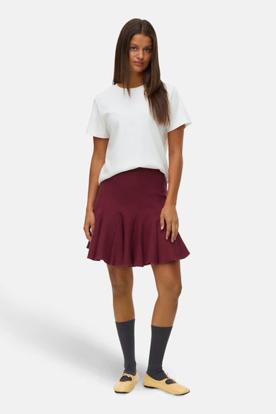 Korte bordeaux rok van VERO MODA®, met een uitlopende pasvorm en gedragen met een wit t-shirt en Mary Jane schoenen.
