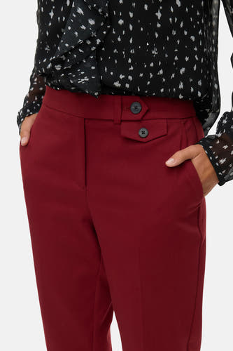 Rode broek van VERO MODA, met decoratieve knopen en zakken, gecombineerd met een zwart-wit geprint bloesje.
