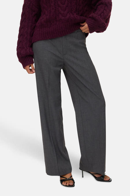 Grijze broek van VERO MODA®, gecombineerd met een gebreide trui en zwarte open schoenen met hak.
