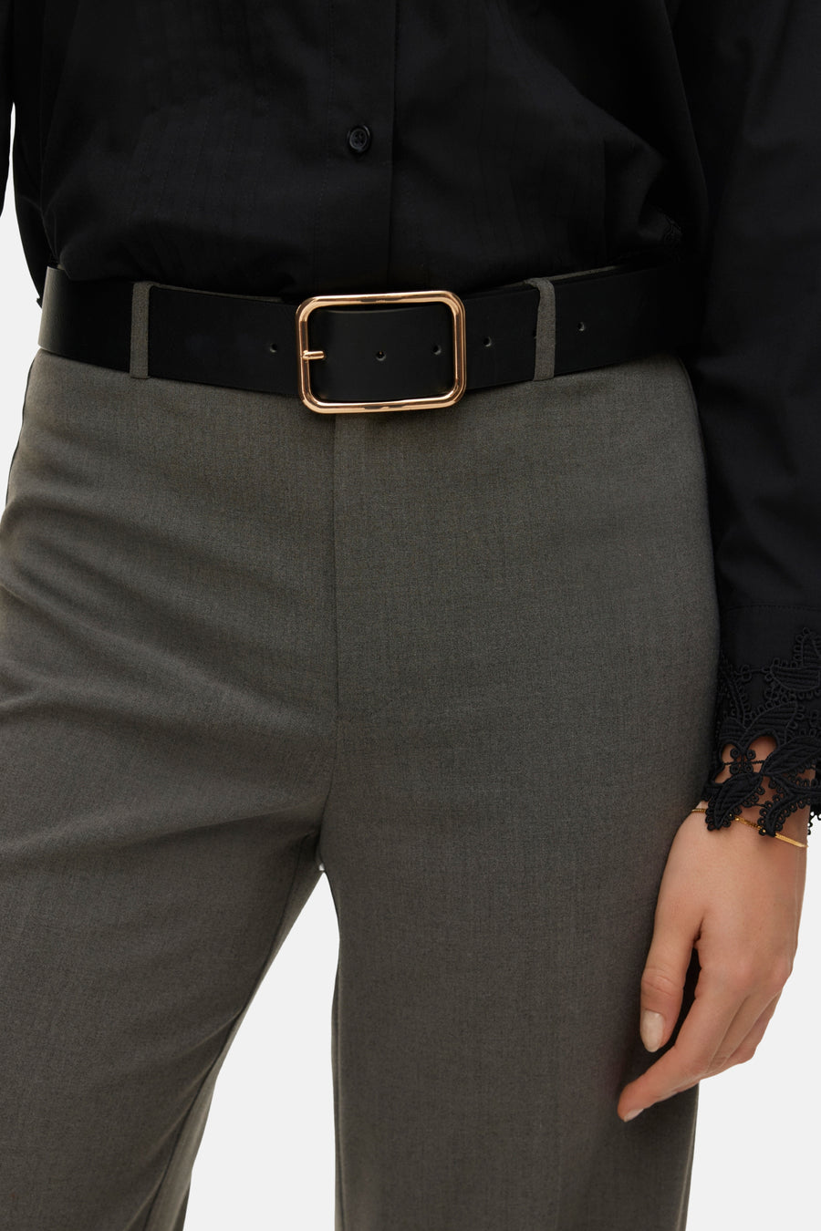 Grijze broek van VERO MODA, met een zwarte riem met gouden gesp en een zwarte blouse met kanten mouw.