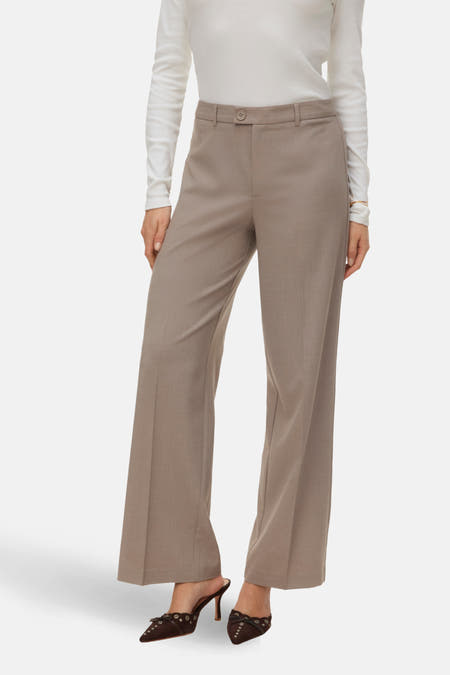Pantalon beige de VERO MODA, avec des longues jambes et porté avec une blouse blanche.