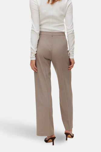 Achterkant van een vrouw in een witte blouse en beige pantalon.