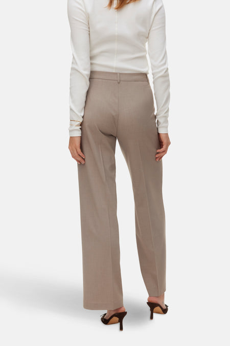 Achterkant van een vrouw in een witte blouse en beige pantalon.