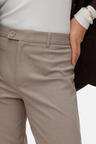 Beige pantalon, witte top, gouden armband.
